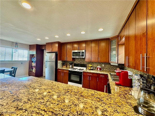 kitchen with kitchen peninsula, appliances with stainless steel finishes, tasteful backsplash, light stone countertops, and sink