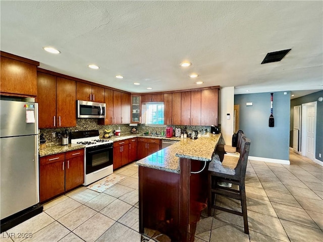 kitchen featuring kitchen peninsula, light tile patterned floors, stainless steel appliances, and a breakfast bar area