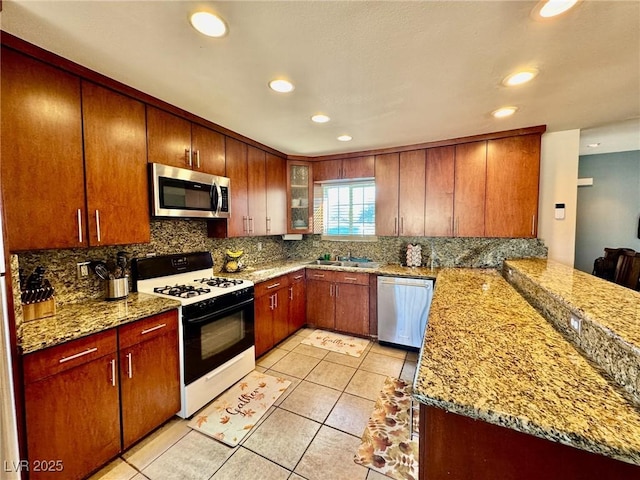 kitchen featuring appliances with stainless steel finishes, sink, light tile patterned floors, kitchen peninsula, and light stone countertops