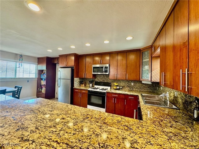 kitchen with sink, backsplash, stainless steel appliances, kitchen peninsula, and dark stone counters