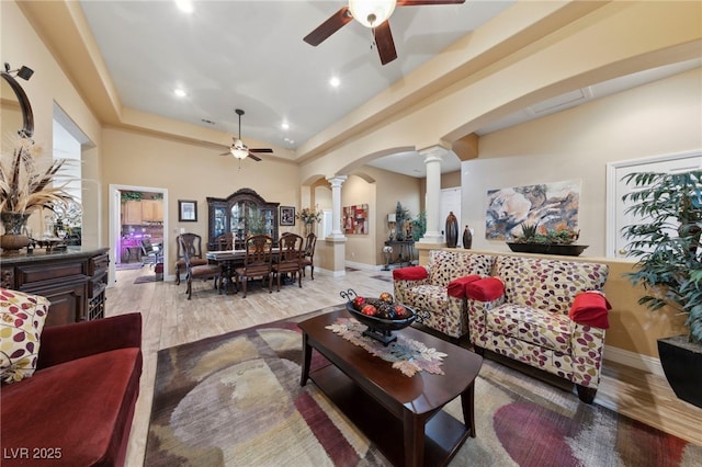 living room with decorative columns, ceiling fan, hardwood / wood-style floors, and a towering ceiling