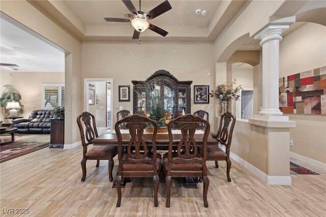 dining space featuring light wood-type flooring, a tray ceiling, and decorative columns