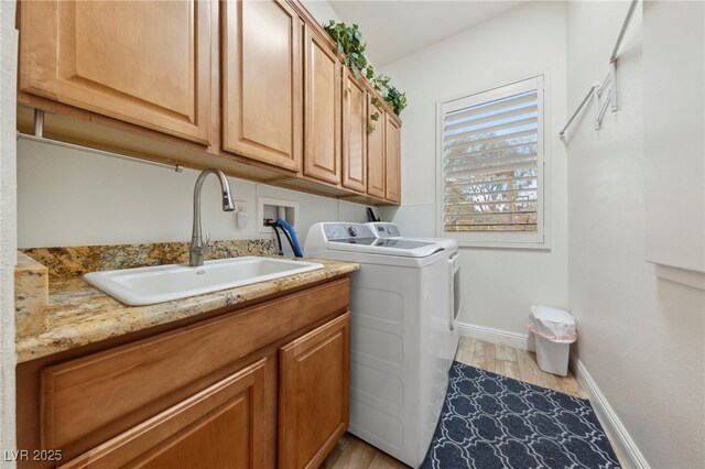 washroom featuring cabinets, sink, washing machine and dryer, and light wood-type flooring