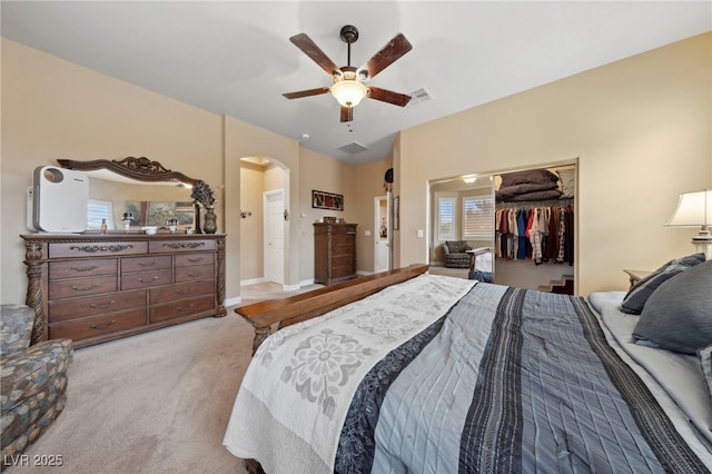 bedroom featuring ceiling fan, light carpet, a closet, and a walk in closet