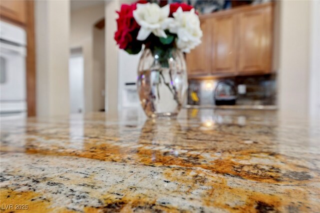 interior details with light brown cabinetry, light stone countertops, and oven