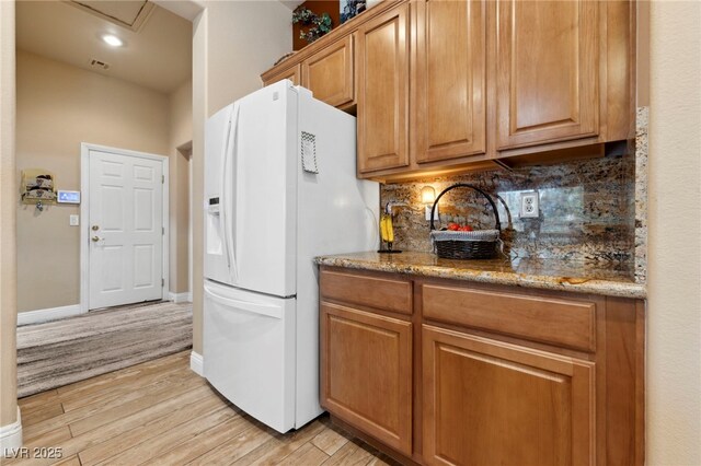 kitchen featuring stone counters, white refrigerator with ice dispenser, light hardwood / wood-style flooring, and tasteful backsplash