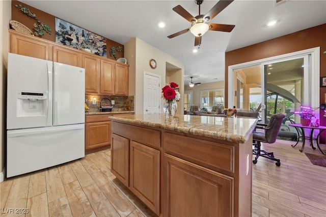 kitchen featuring backsplash, light wood-type flooring, white fridge with ice dispenser, light stone countertops, and a center island