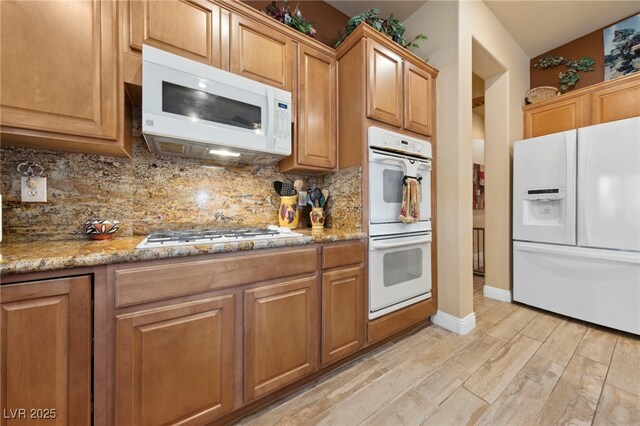 kitchen featuring light stone counters, white appliances, light wood-type flooring, and tasteful backsplash