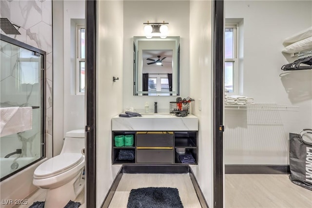 full bathroom with hardwood / wood-style flooring, combined bath / shower with glass door, vanity, and toilet