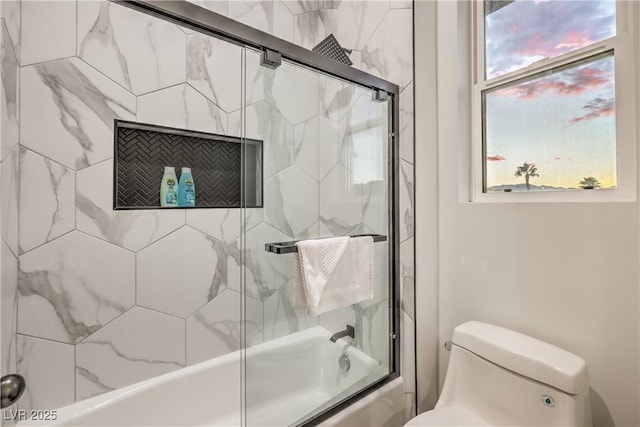 bathroom featuring toilet and bath / shower combo with glass door