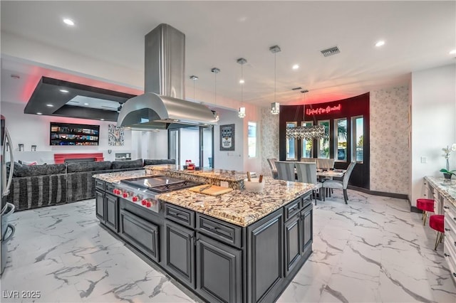 kitchen featuring island exhaust hood, decorative light fixtures, stainless steel gas cooktop, light stone countertops, and a kitchen island