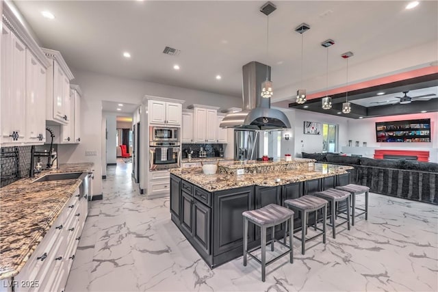 kitchen featuring decorative light fixtures, a spacious island, island exhaust hood, white cabinetry, and appliances with stainless steel finishes