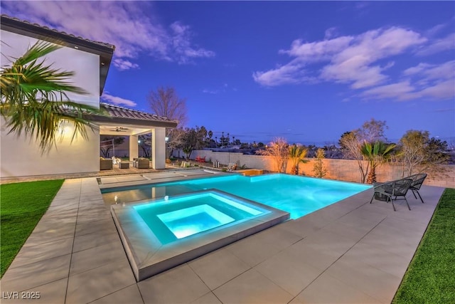 pool at dusk featuring a patio area and an in ground hot tub