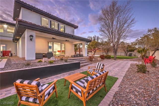 back house at dusk with ceiling fan, a patio area, and an outdoor living space