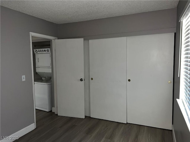 unfurnished bedroom with dark wood-type flooring, a textured ceiling, a closet, and stacked washing maching and dryer