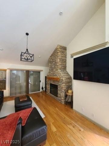 living room featuring hardwood / wood-style floors, a notable chandelier, lofted ceiling, and a stone fireplace