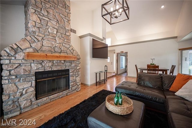 living room featuring high vaulted ceiling, a notable chandelier, a stone fireplace, and hardwood / wood-style flooring