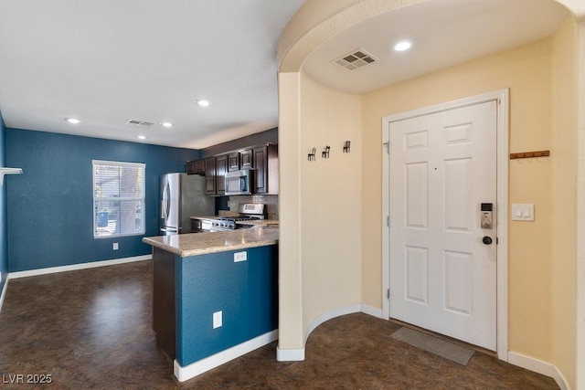 kitchen with appliances with stainless steel finishes, backsplash, kitchen peninsula, and dark brown cabinetry