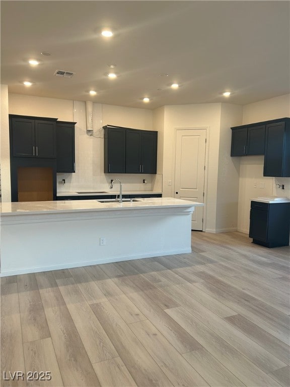 kitchen featuring sink, backsplash, a kitchen island with sink, and light hardwood / wood-style floors