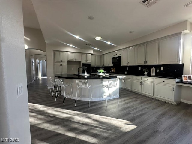 kitchen with an island with sink, tasteful backsplash, dark hardwood / wood-style flooring, vaulted ceiling, and a breakfast bar