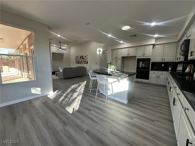 kitchen featuring a kitchen bar, hardwood / wood-style floors, backsplash, white cabinets, and black appliances