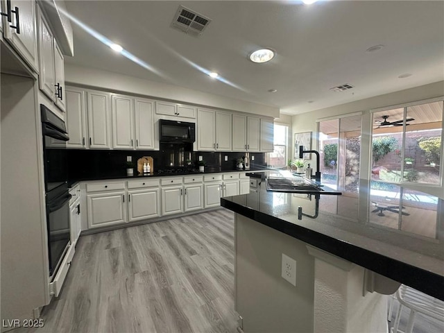 kitchen with kitchen peninsula, decorative backsplash, black appliances, light hardwood / wood-style flooring, and sink