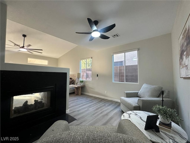 bedroom featuring ceiling fan, light hardwood / wood-style floors, a multi sided fireplace, and lofted ceiling