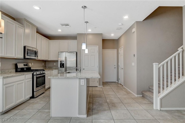 kitchen with stainless steel appliances, a kitchen island with sink, light tile patterned flooring, hanging light fixtures, and light stone counters