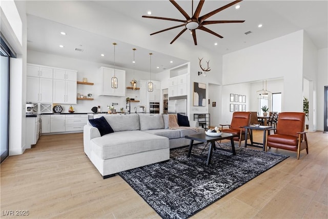 living room featuring ceiling fan with notable chandelier, light hardwood / wood-style flooring, and a high ceiling