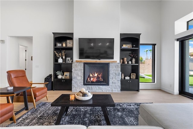 living room featuring light wood-type flooring, built in shelves, a stone fireplace, and a towering ceiling