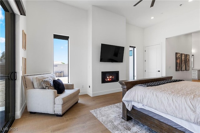 bedroom with ceiling fan, light hardwood / wood-style flooring, and a towering ceiling