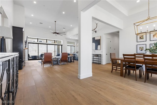 interior space with ceiling fan with notable chandelier, a high ceiling, pendant lighting, and light wood-type flooring