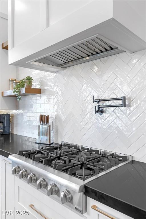 interior details featuring custom exhaust hood, white cabinetry, stainless steel gas stovetop, and tasteful backsplash