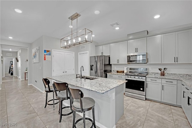 kitchen with light stone countertops, appliances with stainless steel finishes, sink, and a center island with sink