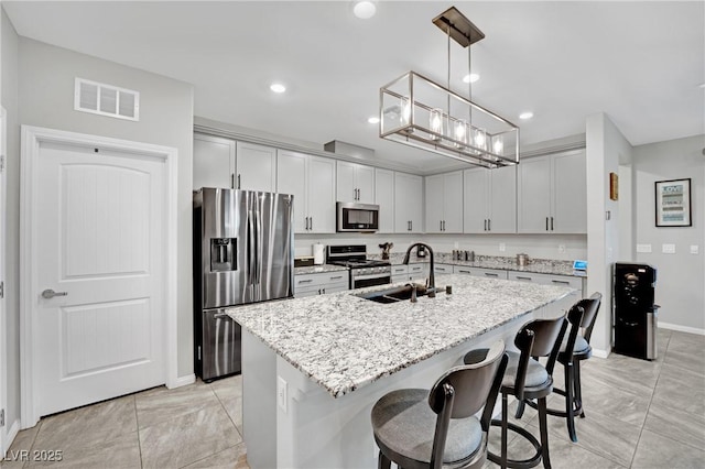 kitchen featuring appliances with stainless steel finishes, sink, hanging light fixtures, a kitchen island with sink, and light stone counters