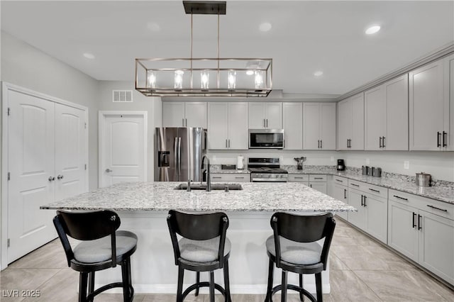 kitchen featuring light stone countertops, appliances with stainless steel finishes, decorative light fixtures, sink, and a kitchen island with sink