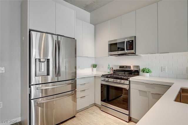 kitchen featuring white cabinets, appliances with stainless steel finishes, tasteful backsplash, and light wood-type flooring