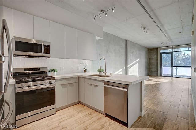 kitchen with white cabinets, appliances with stainless steel finishes, light hardwood / wood-style floors, sink, and kitchen peninsula