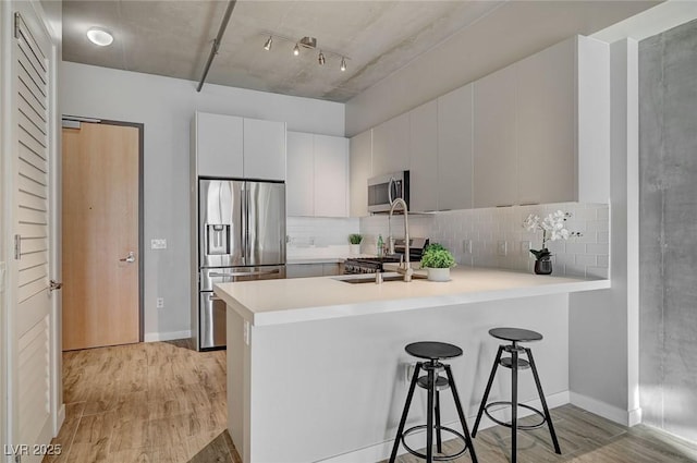 kitchen featuring kitchen peninsula, appliances with stainless steel finishes, light wood-type flooring, a kitchen breakfast bar, and white cabinets