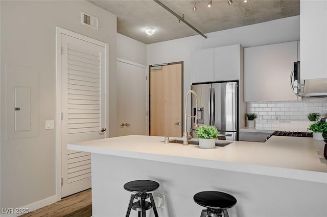 kitchen featuring electric panel, kitchen peninsula, stainless steel refrigerator with ice dispenser, a breakfast bar area, and white cabinets