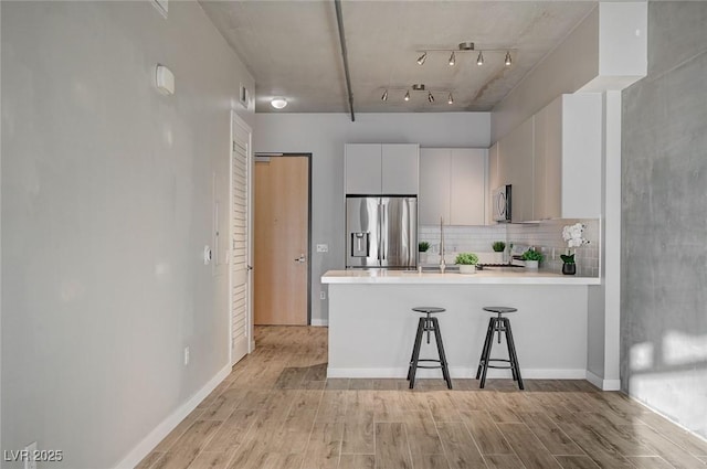 kitchen featuring white cabinetry, kitchen peninsula, appliances with stainless steel finishes, tasteful backsplash, and a breakfast bar