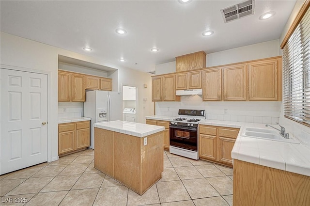 kitchen featuring independent washer and dryer, a center island, light tile patterned flooring, sink, and white appliances