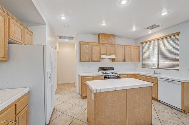 kitchen with tile countertops, light brown cabinets, white appliances, and a center island