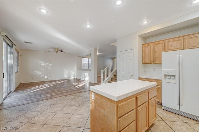 kitchen featuring white fridge with ice dispenser, a center island, tile counters, light tile patterned flooring, and ceiling fan