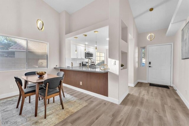 dining space featuring high vaulted ceiling, sink, and light hardwood / wood-style floors