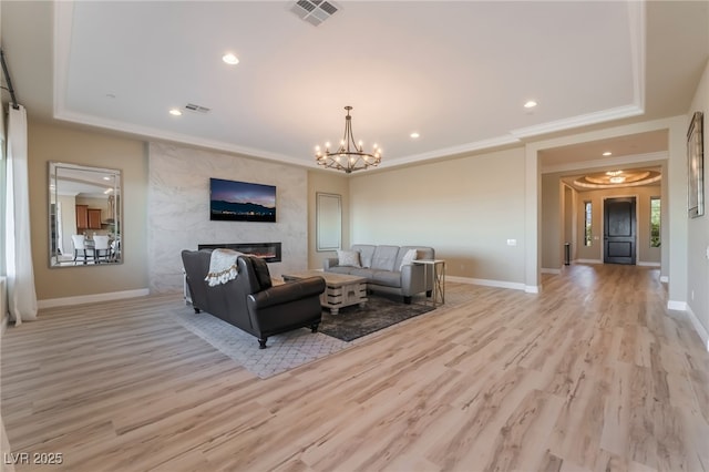 living room featuring light wood-type flooring, a premium fireplace, an inviting chandelier, and a tray ceiling