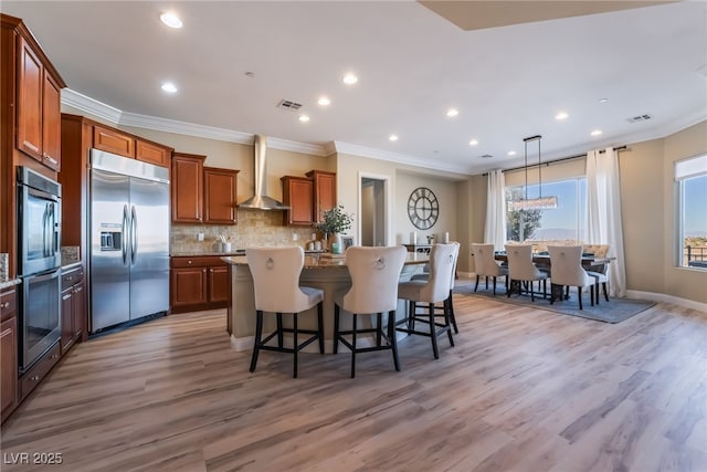 kitchen with light hardwood / wood-style floors, a kitchen island, a breakfast bar, stainless steel appliances, and wall chimney exhaust hood