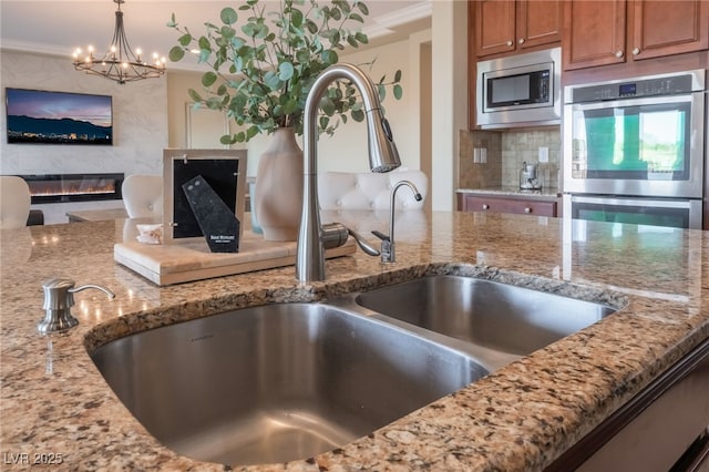 kitchen with hanging light fixtures, appliances with stainless steel finishes, sink, light stone countertops, and a premium fireplace