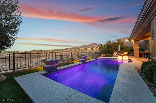 pool at dusk with a patio area and pool water feature