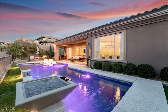 pool at dusk featuring ceiling fan, a patio, outdoor lounge area, and a hot tub